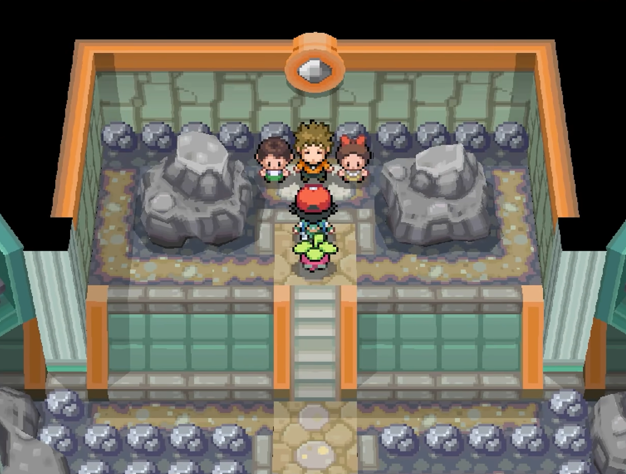 The player stands among trainers and large rocks inside a tiled room.